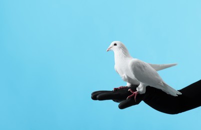 Photo of Woman with beautiful white dove on light blue background, closeup. Space for text