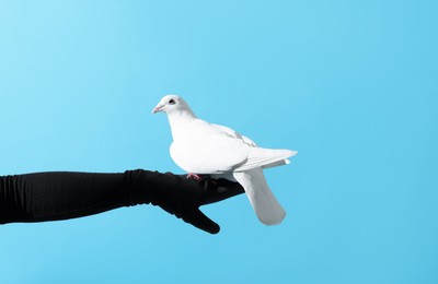 Photo of Woman with beautiful white dove on light blue background, closeup