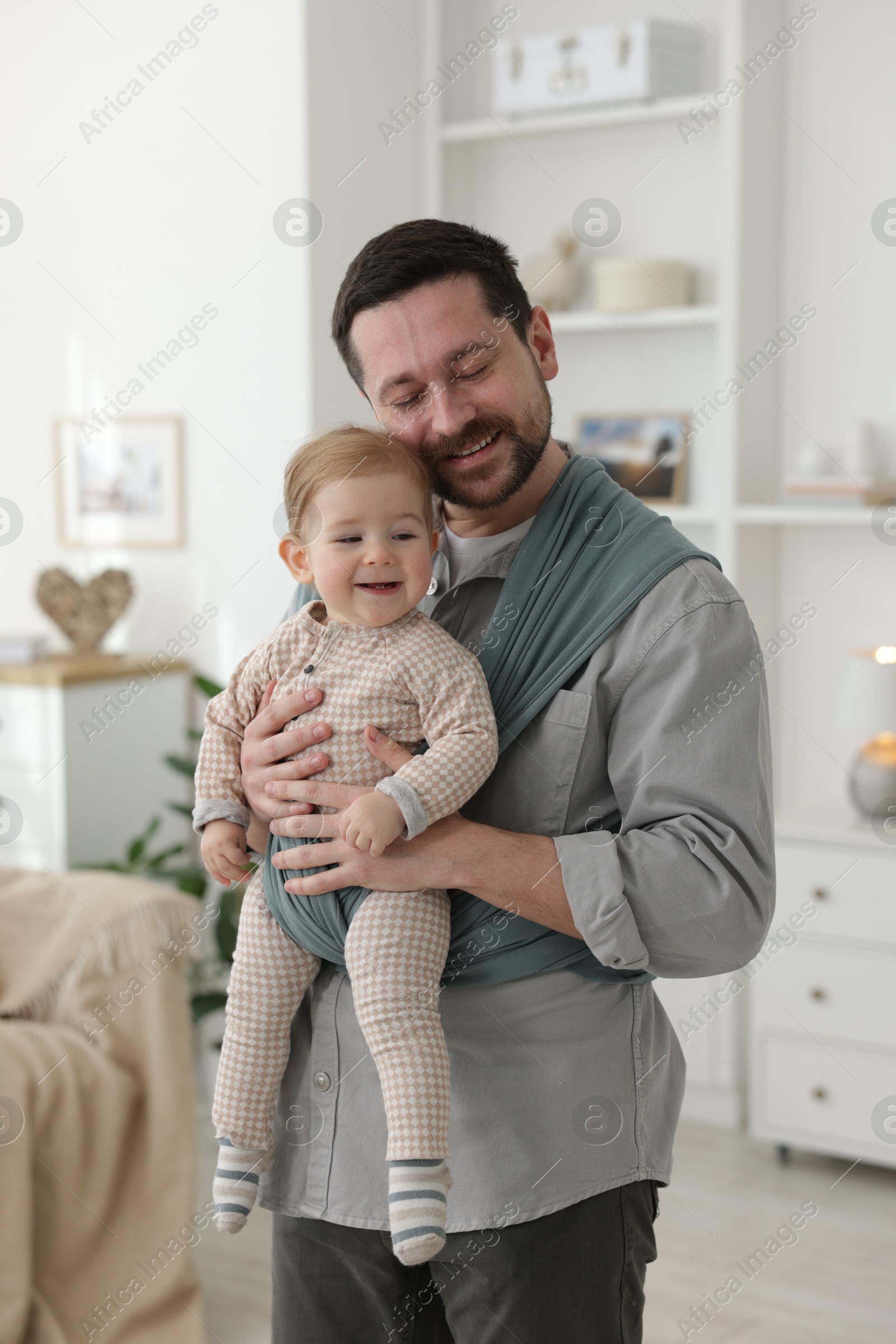 Photo of Father holding his child in sling (baby carrier) at home