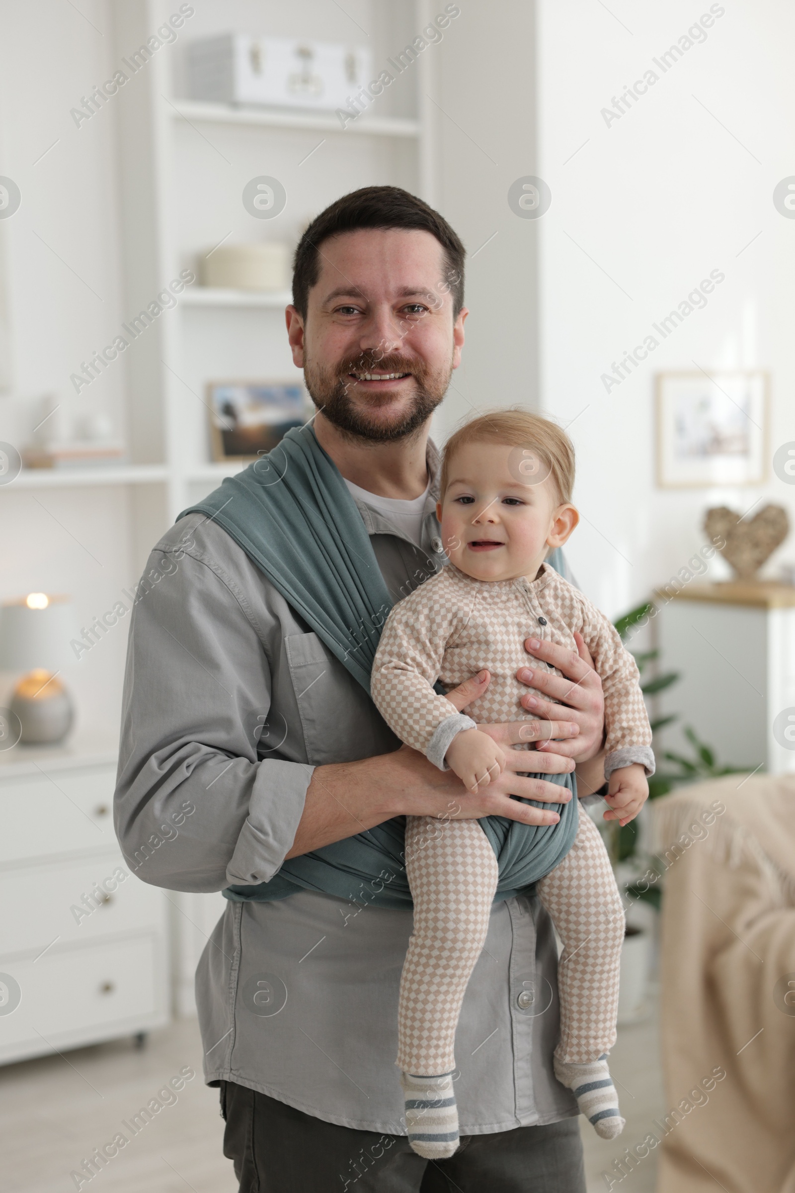 Photo of Father holding his child in sling (baby carrier) at home