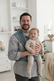 Father holding his child in sling (baby carrier) at home