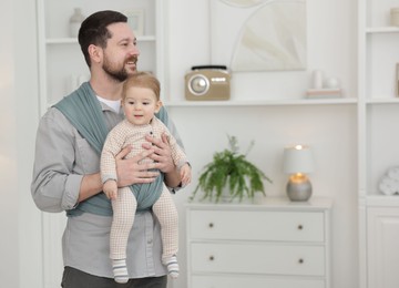 Photo of Father holding his child in sling (baby carrier) at home, space for text