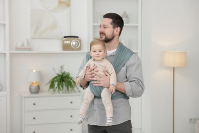 Father holding his child in sling (baby carrier) at home