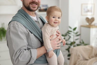 Photo of Father holding his child in sling (baby carrier) at home, closeup. Space for text