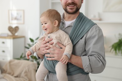 Father holding his child in sling (baby carrier) at home, closeup