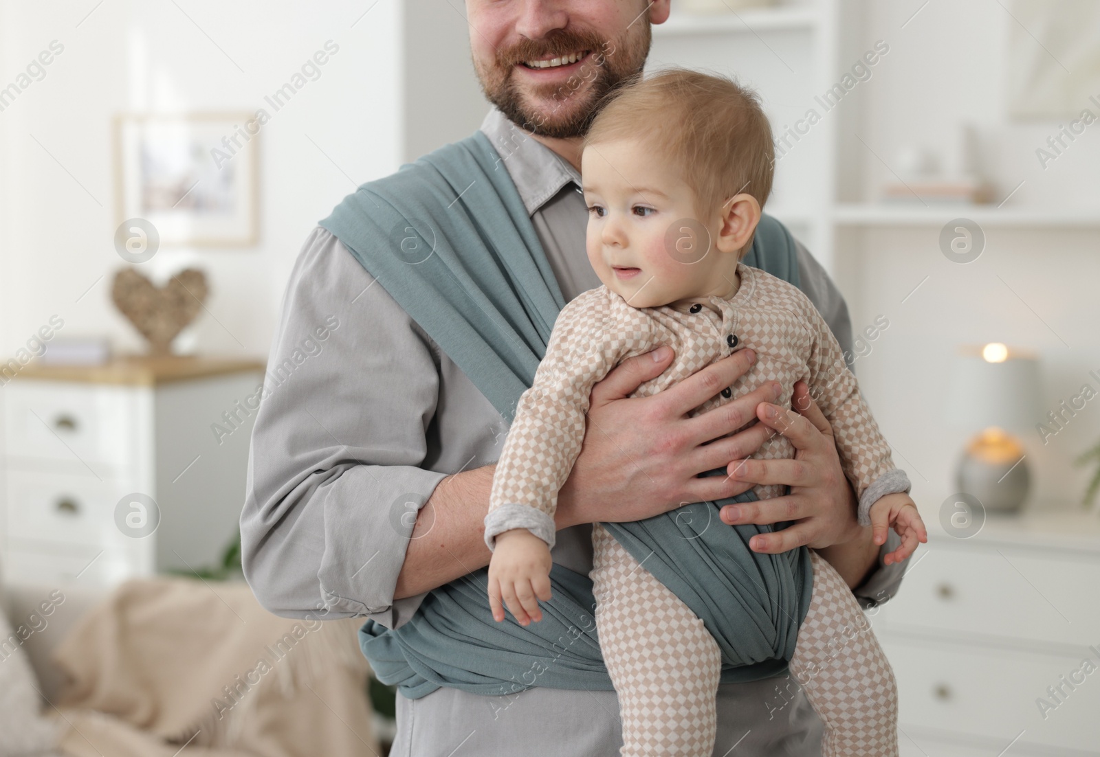 Photo of Father holding his child in sling (baby carrier) at home, closeup