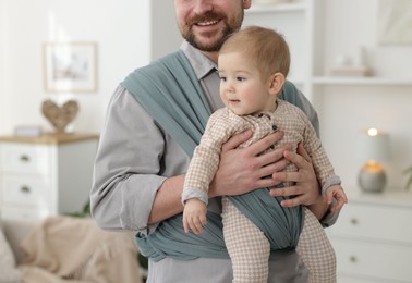 Photo of Father holding his child in sling (baby carrier) at home, closeup