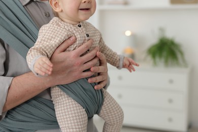 Father holding his child in sling (baby carrier) at home, closeup. Space for text