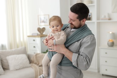 Father holding his child in sling (baby carrier) at home, space for text