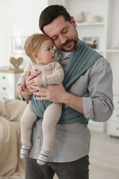 Father holding his child in sling (baby carrier) at home