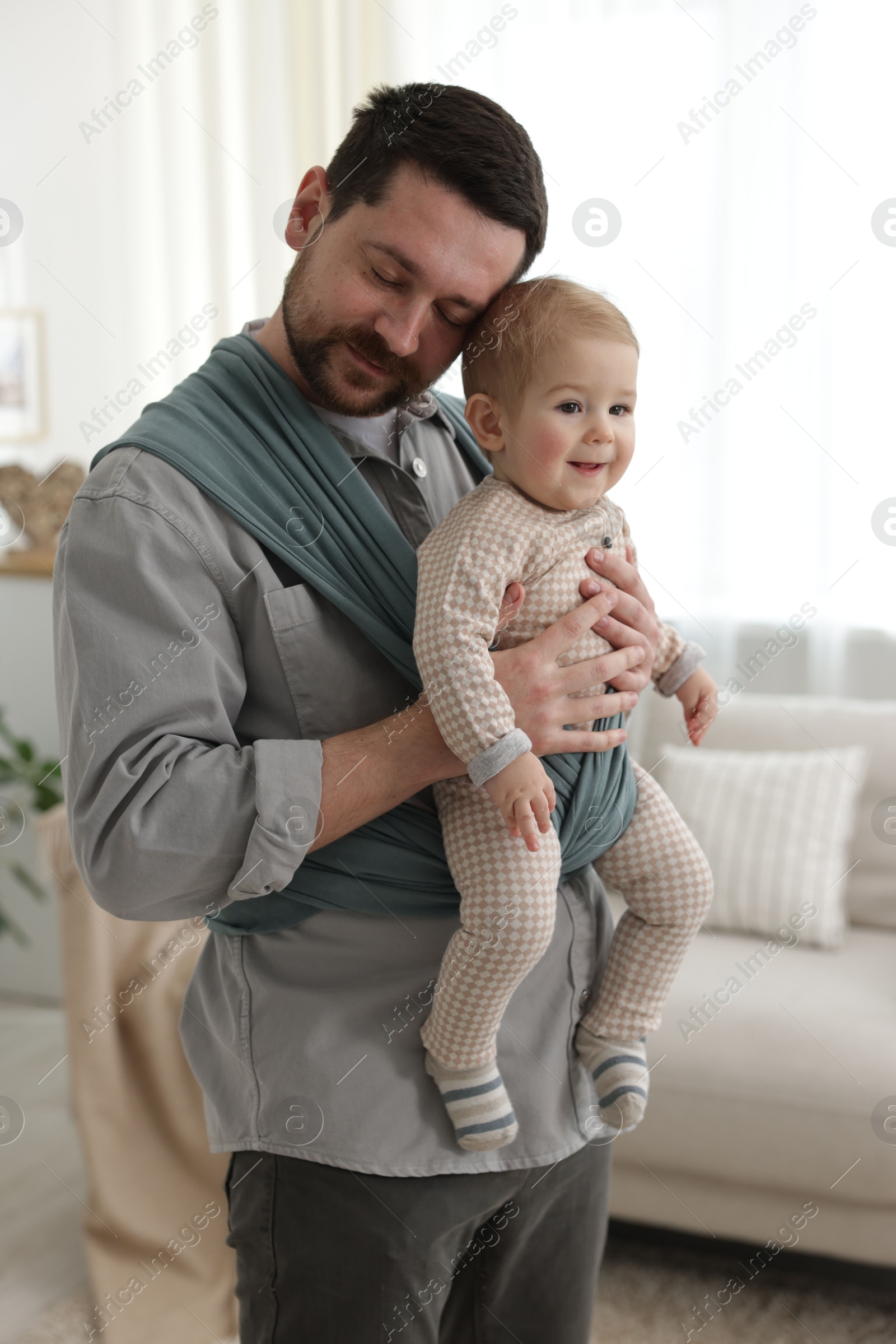 Photo of Father holding his child in sling (baby carrier) at home