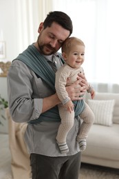 Father holding his child in sling (baby carrier) at home