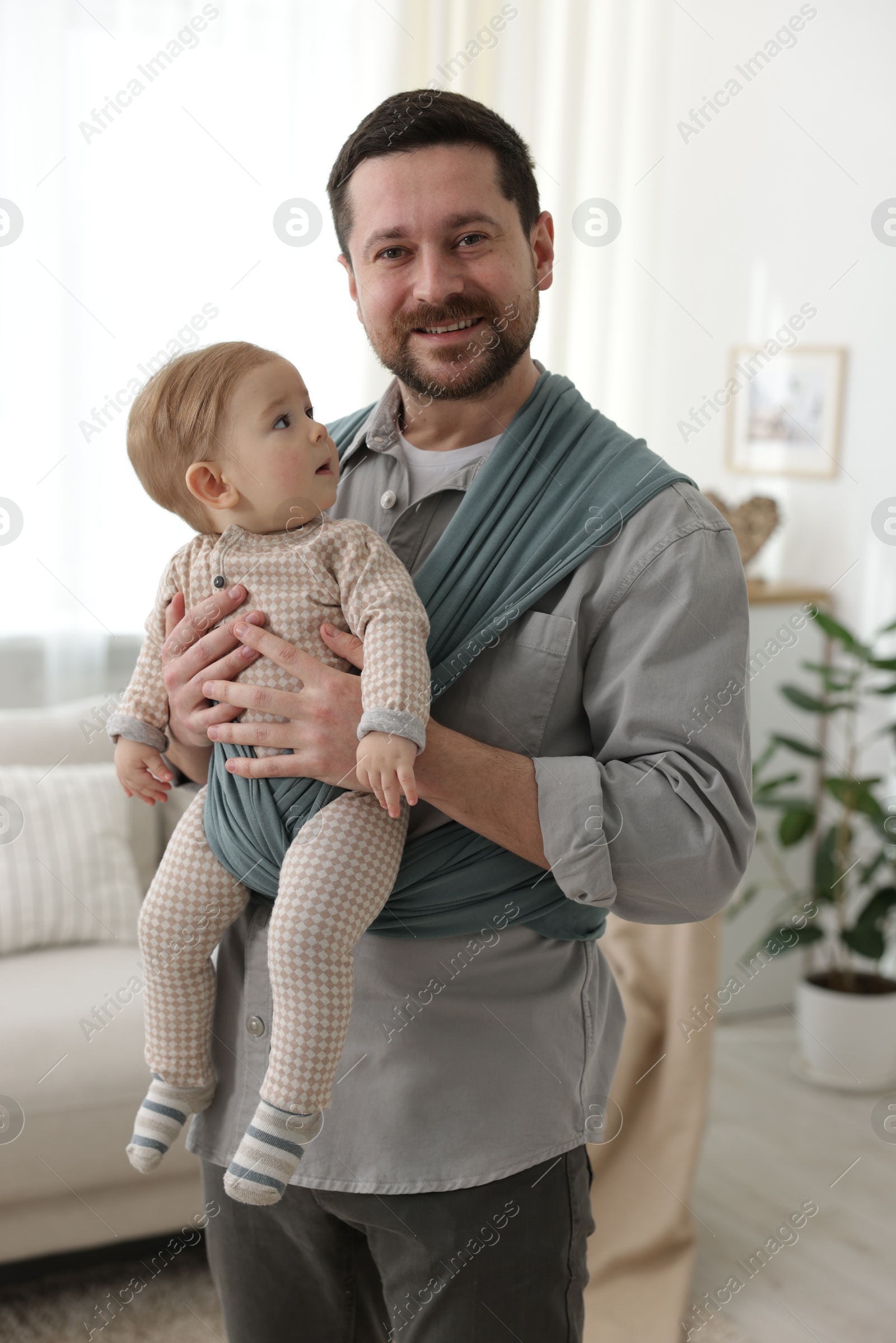 Photo of Father holding his child in sling (baby carrier) at home