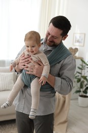 Father holding his child in sling (baby carrier) at home