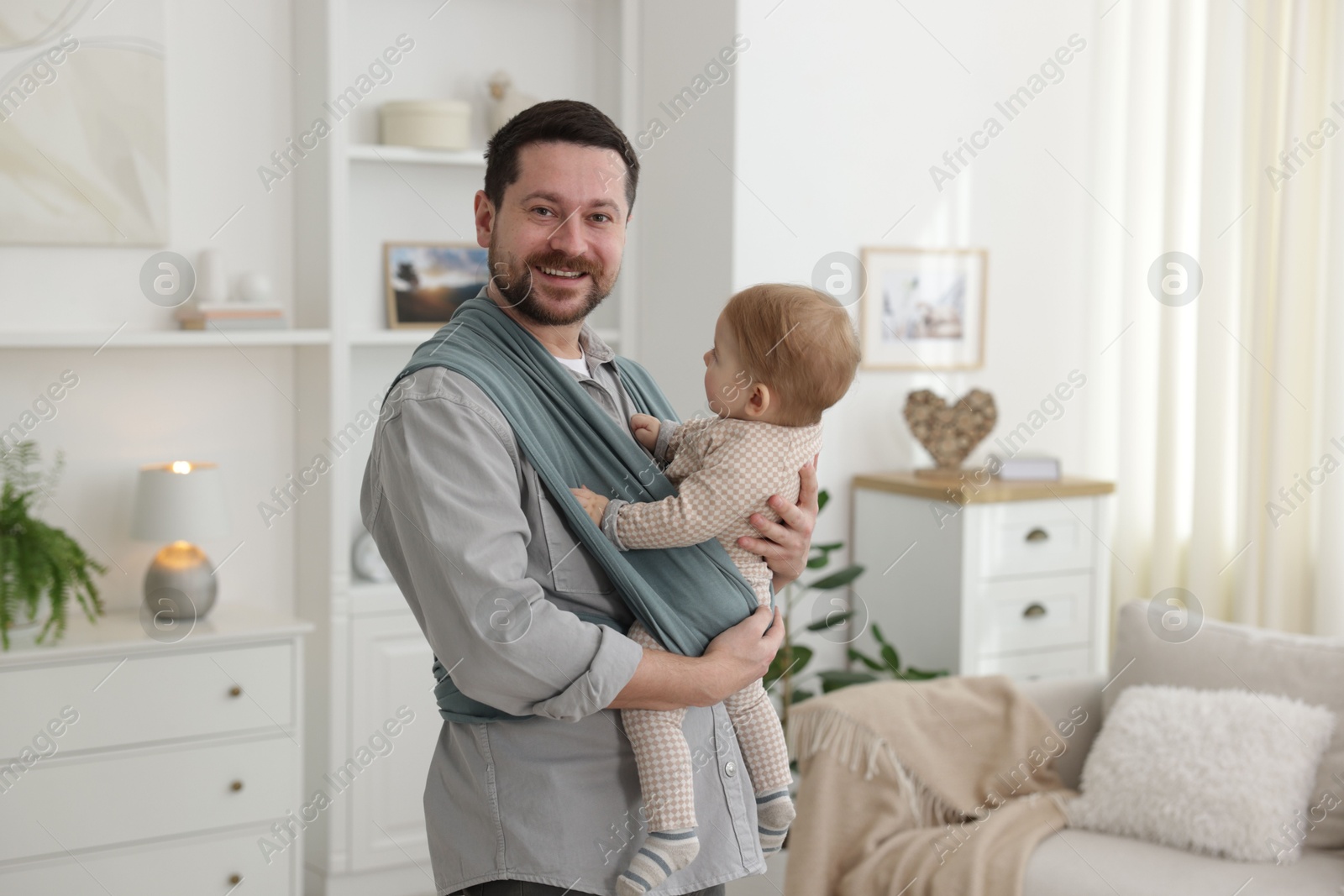 Photo of Father holding his child in sling (baby carrier) at home