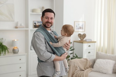 Photo of Father holding his child in sling (baby carrier) at home