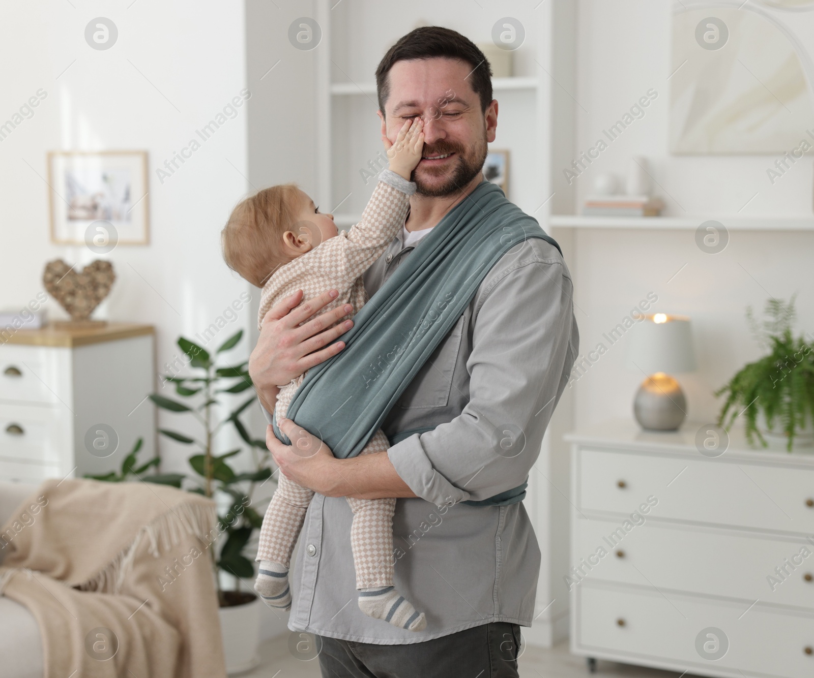 Father holding his child in sling (baby carrier) at home Photo of Father holding his child in sling (baby carrier) at home
