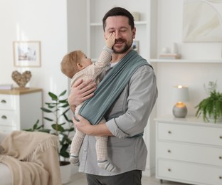 Photo of Father holding his child in sling (baby carrier) at home