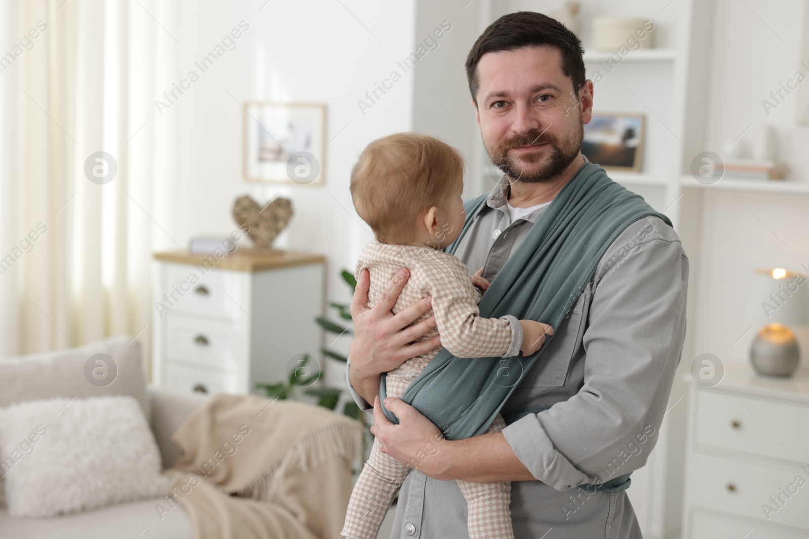 Photo of Father holding his child in sling (baby carrier) at home, space for text