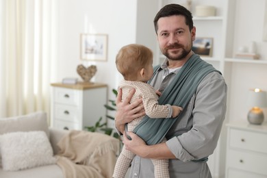 Photo of Father holding his child in sling (baby carrier) at home, space for text