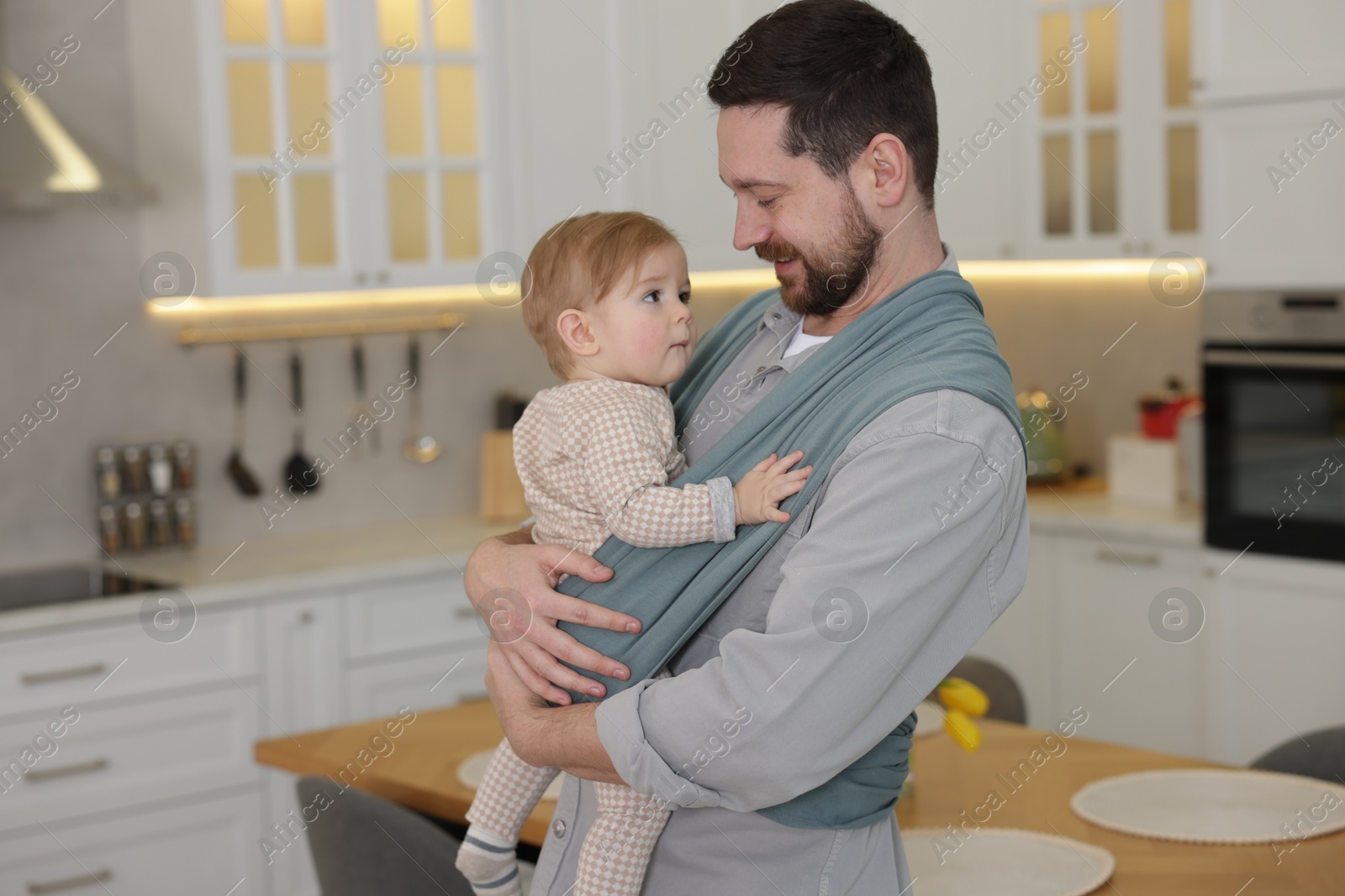 Photo of Father holding his child in sling (baby carrier) at home