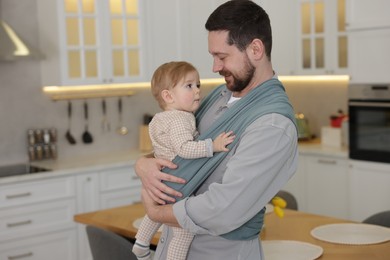 Father holding his child in sling (baby carrier) at home