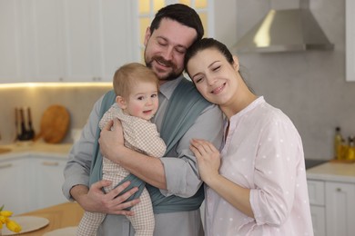 Portrait of happy family indoors. Father holding his child in sling (baby carrier) at home