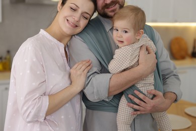 Photo of Parents with their baby indoors. Father holding his child in sling at home, closeup