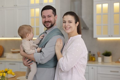 Portrait of happy family indoors. Father holding his child in sling (baby carrier) at home