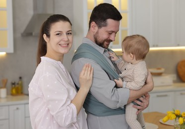 Portrait of happy family indoors. Father holding his child in sling (baby carrier) at home