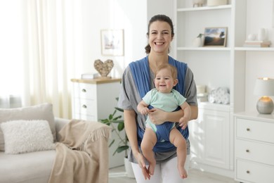 Mother holding her child in sling at home, space for text