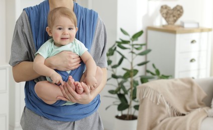 Mother holding her child in sling at home, closeup. Space for text