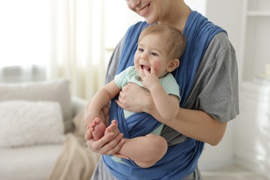 Mother holding her child in sling at home, closeup. Space for text