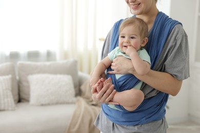 Mother holding her child in sling at home, closeup. Space for text