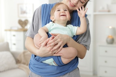 Mother holding her child in sling at home, closeup