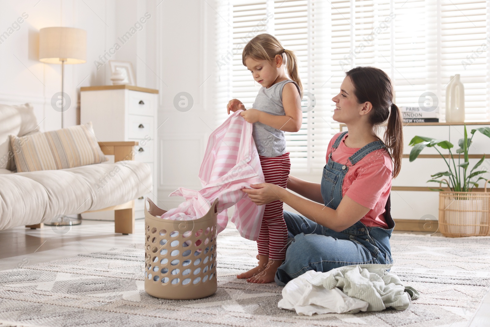 Photo of Little girl helping her mother taking out laundry from basket at home