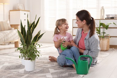 Little helper. Mother and her cute daughter with spray bottle near houseplants at home