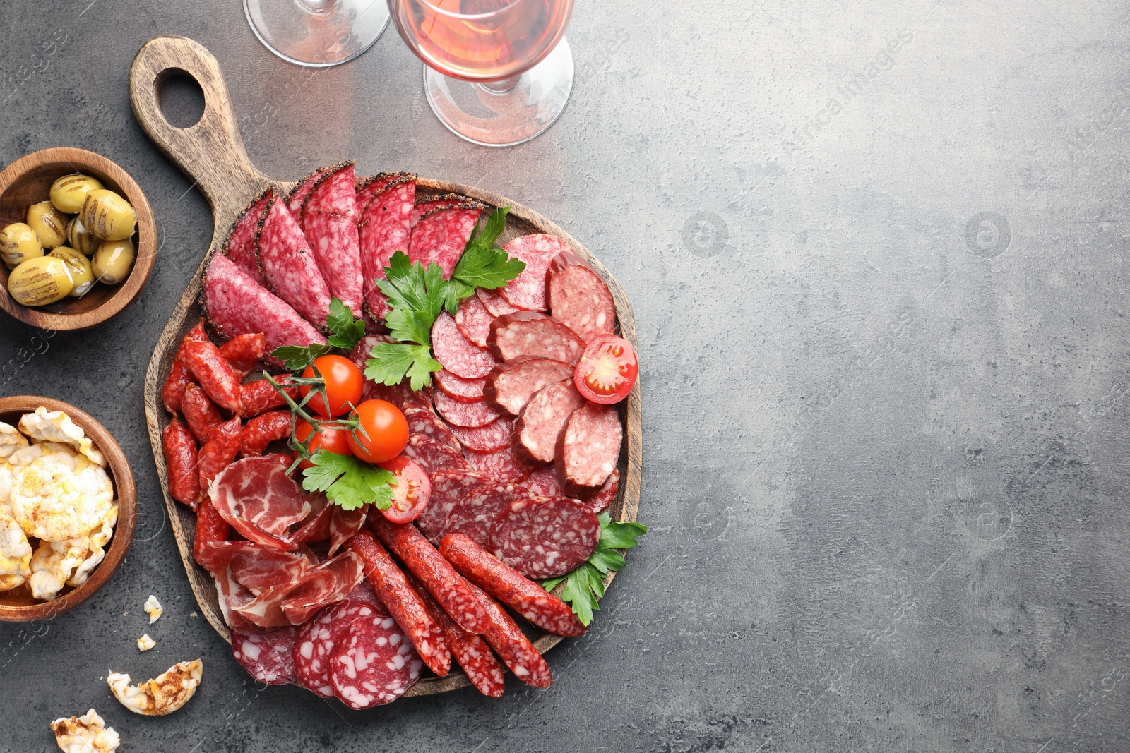 Photo of Different smoked sausages slices served on grey table, flat lay. Space for text