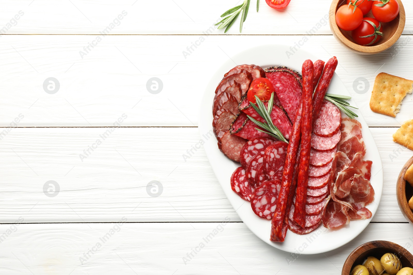 Photo of Different smoked sausages slices served on white wooden table, flat lay. Space for text