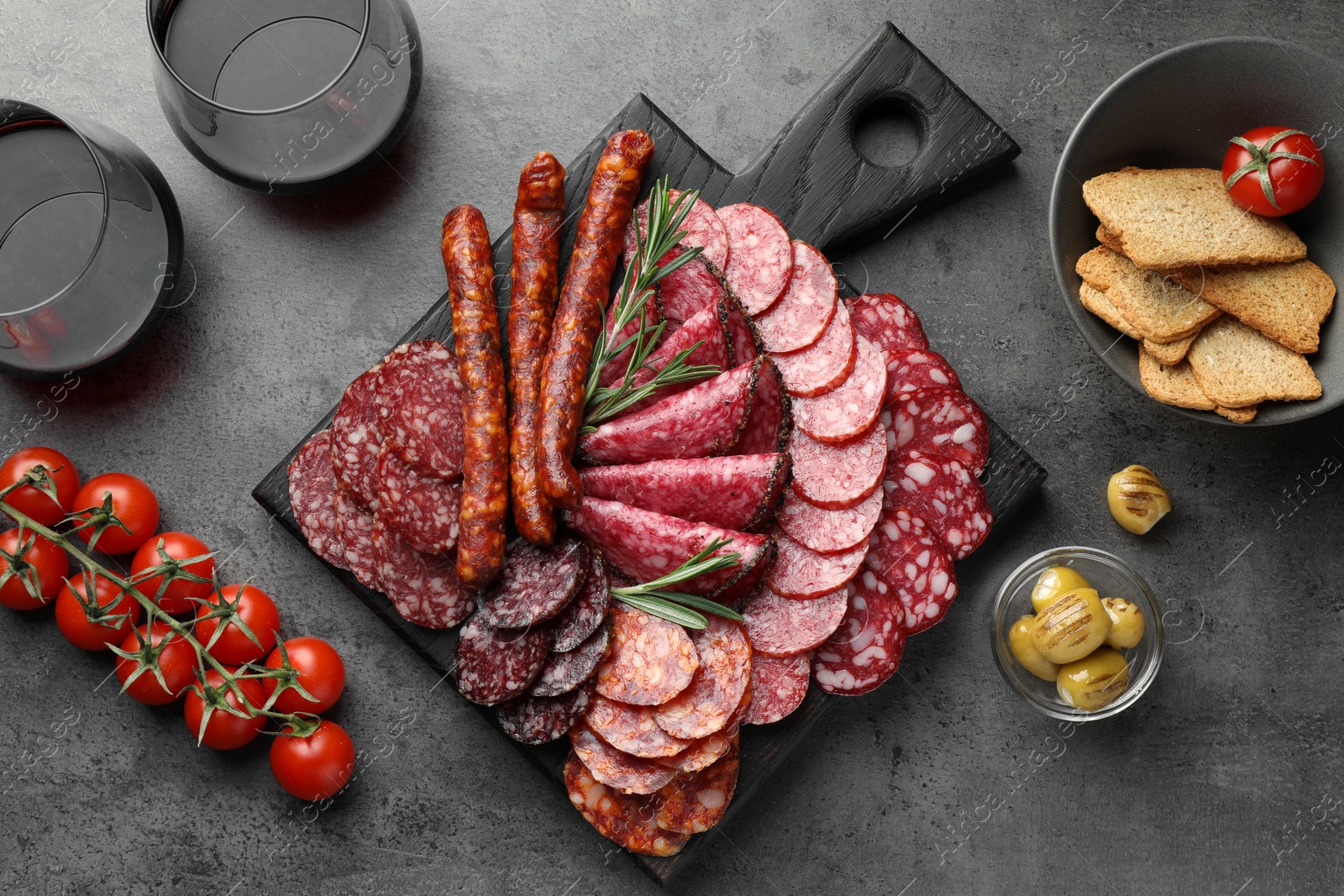 Photo of Different smoked sausages slices served on grey table, flat lay