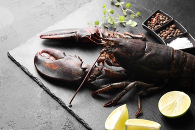 Photo of Raw lobster, cut lime, microgreens and spices on dark textured table, closeup