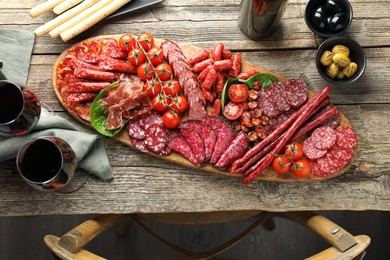 Different smoked sausages and other snacks served with wine on wooden table, flat lay