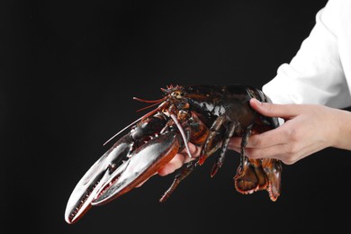 Photo of Woman with raw lobster on black background, closeup