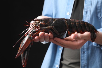 Photo of Man with raw lobster on black background, closeup