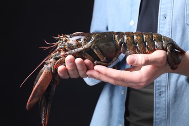 Photo of Man with raw lobster on black background, closeup