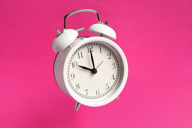 Photo of White alarm clock in air on bright pink background