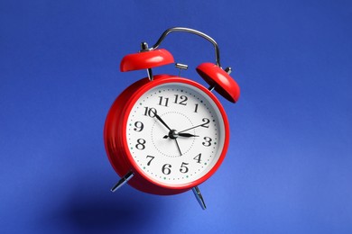 Photo of Red alarm clock in air on blue background