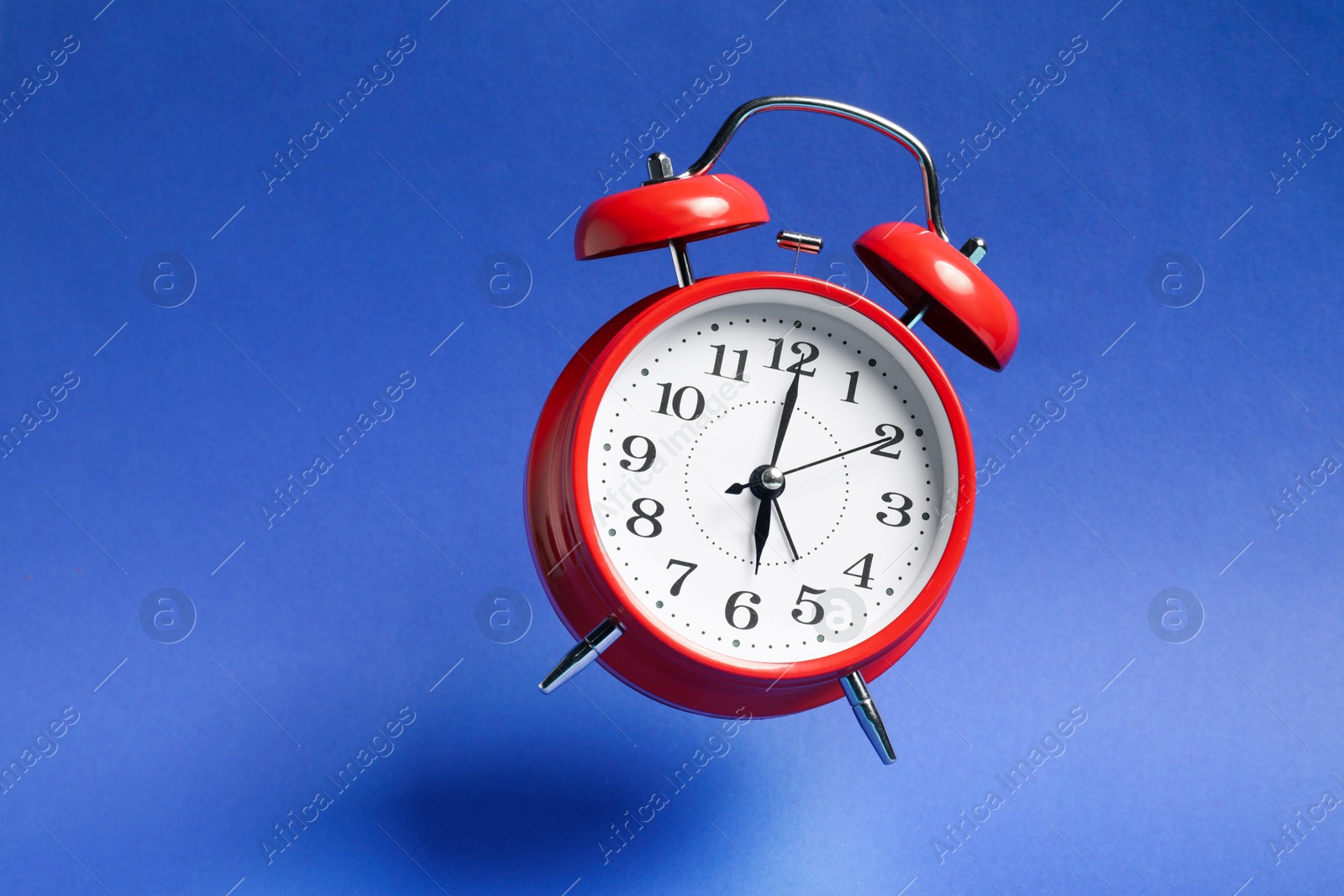 Red alarm clock in air on blue background Photo of Red alarm clock in air on blue background