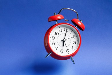 Photo of Red alarm clock in air on blue background
