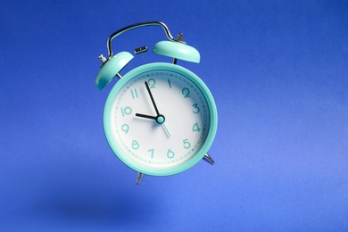 Photo of Turquoise alarm clock in air on blue background